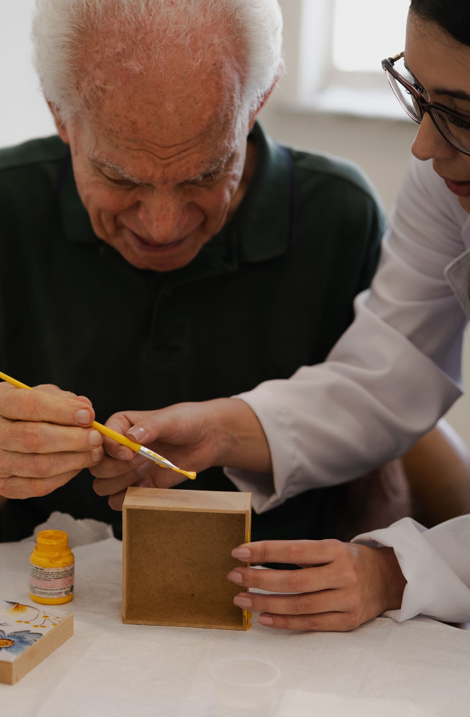 An older man painting with a support worker beside him